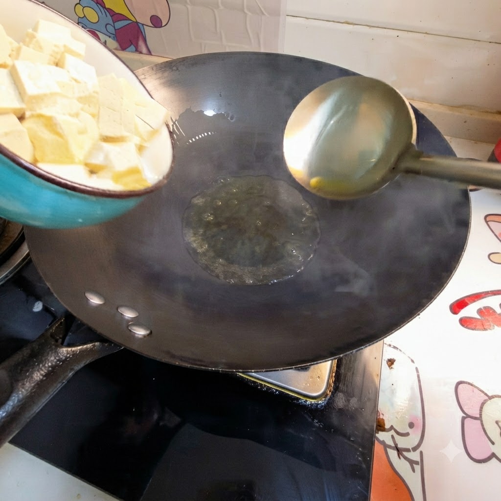 Cubos de tofu vaciándose de un tazón a un wok con aceite caliente.