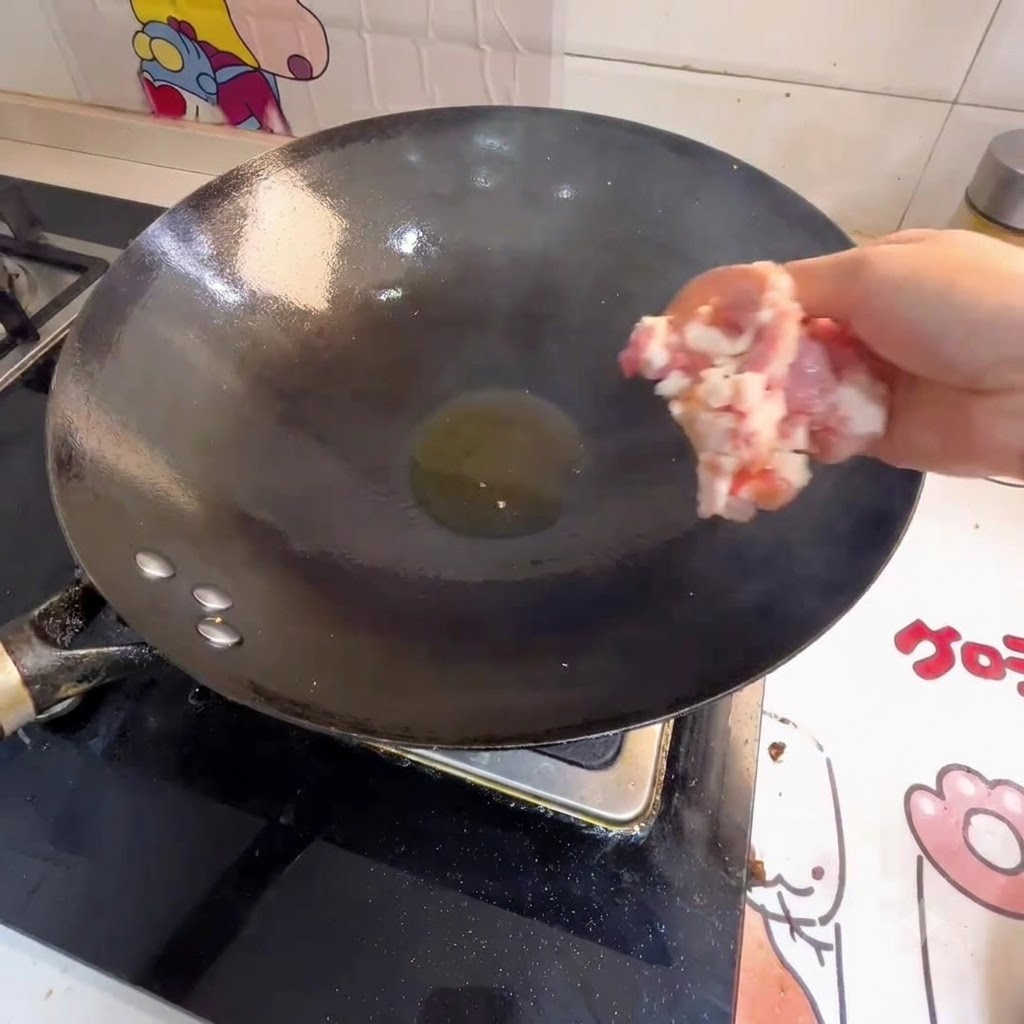 Mano agregando carne picada a un wok con aceite caliente.