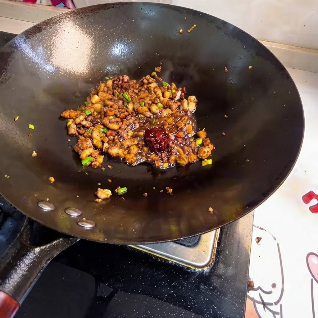 Cucharada de pasta de frijoles sobre la carne salteada en el wok.
