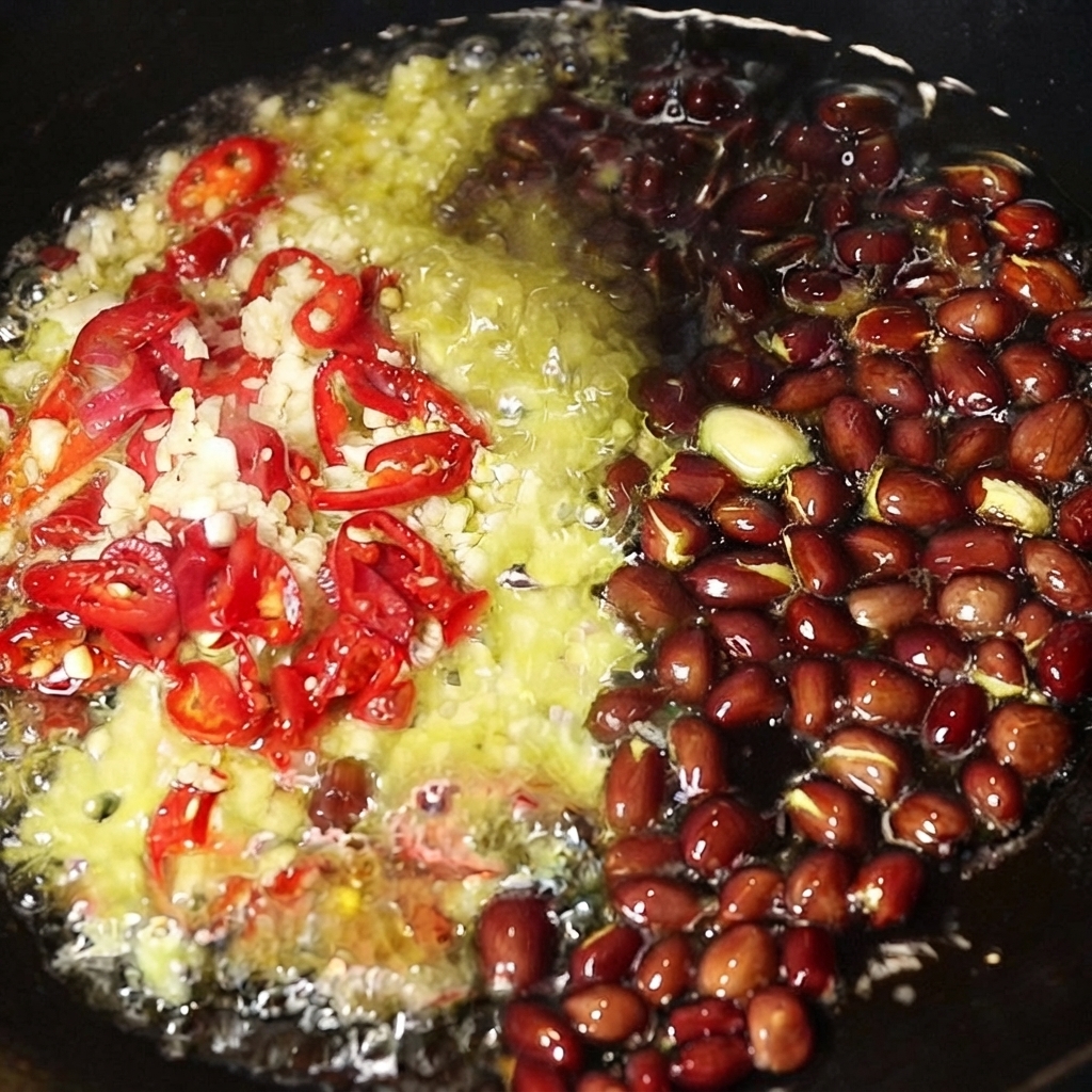 Ajo picado, chiles rojos en rodajas y maní entero chisporroteando en aceite caliente dentro de un wok.