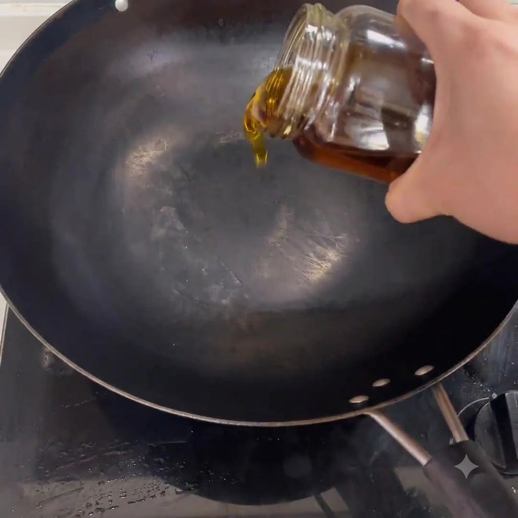 Aceite de cocina cayendo desde un frasco hacia un wok negro colocado sobre una estufa.