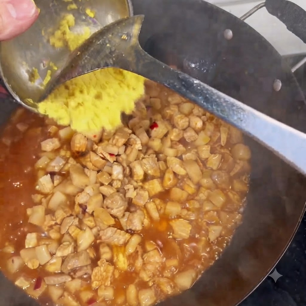 Jengibre picado siendo raspado desde un cucharón hacia un wok lleno de carne y salsa a fuego lento.