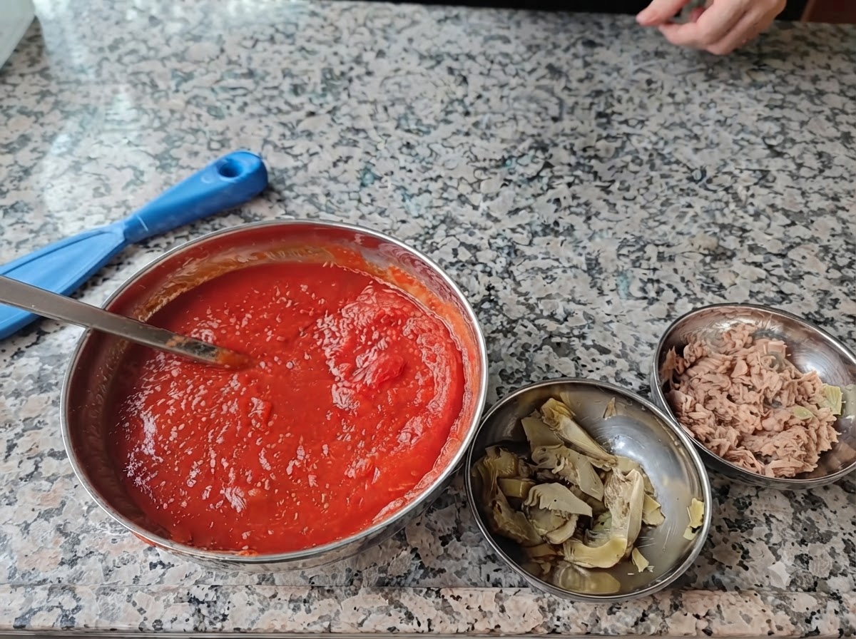 Cuatro cuencos de acero llenos de ingredientes para pizza dispuestos sobre una superficie de mármol.
