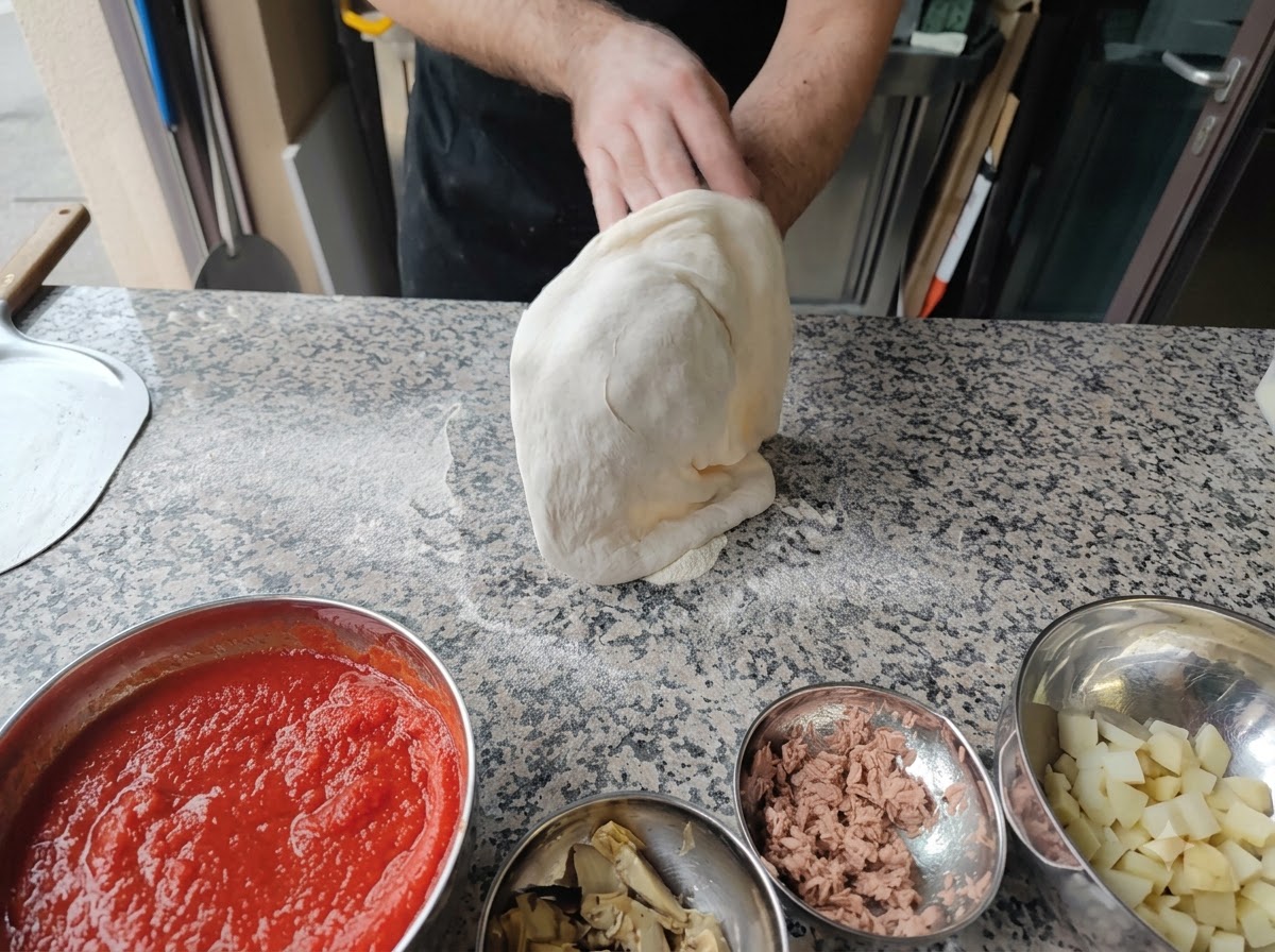 Una persona estirando la masa de pizza sobre sus puños en el aire.