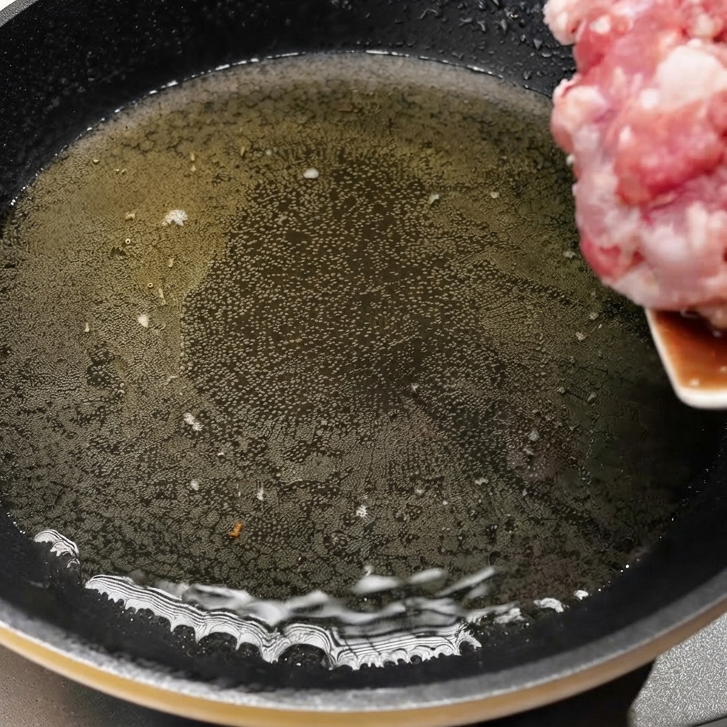 Cerdo picado siendo transferido a una sartén caliente con aceite para comenzar a cocinar.