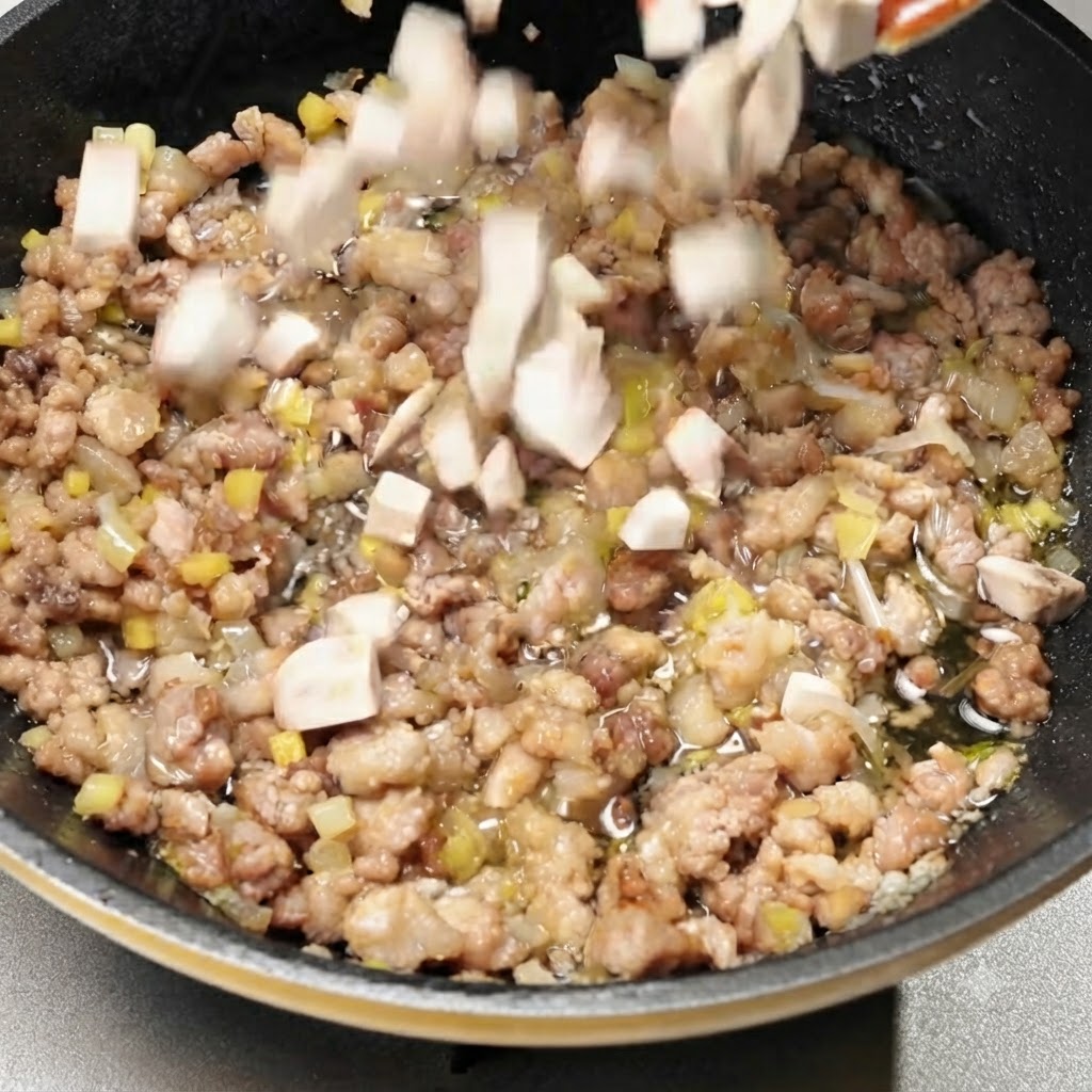 Champiñones picados siendo mezclados en la sartén con la carne de cerdo sazonada.