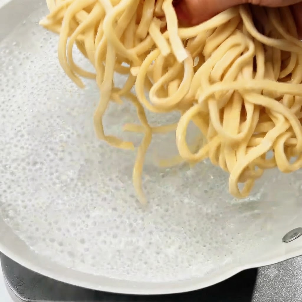 Fideos frescos siendo sumergidos en una olla con agua hirviendo.