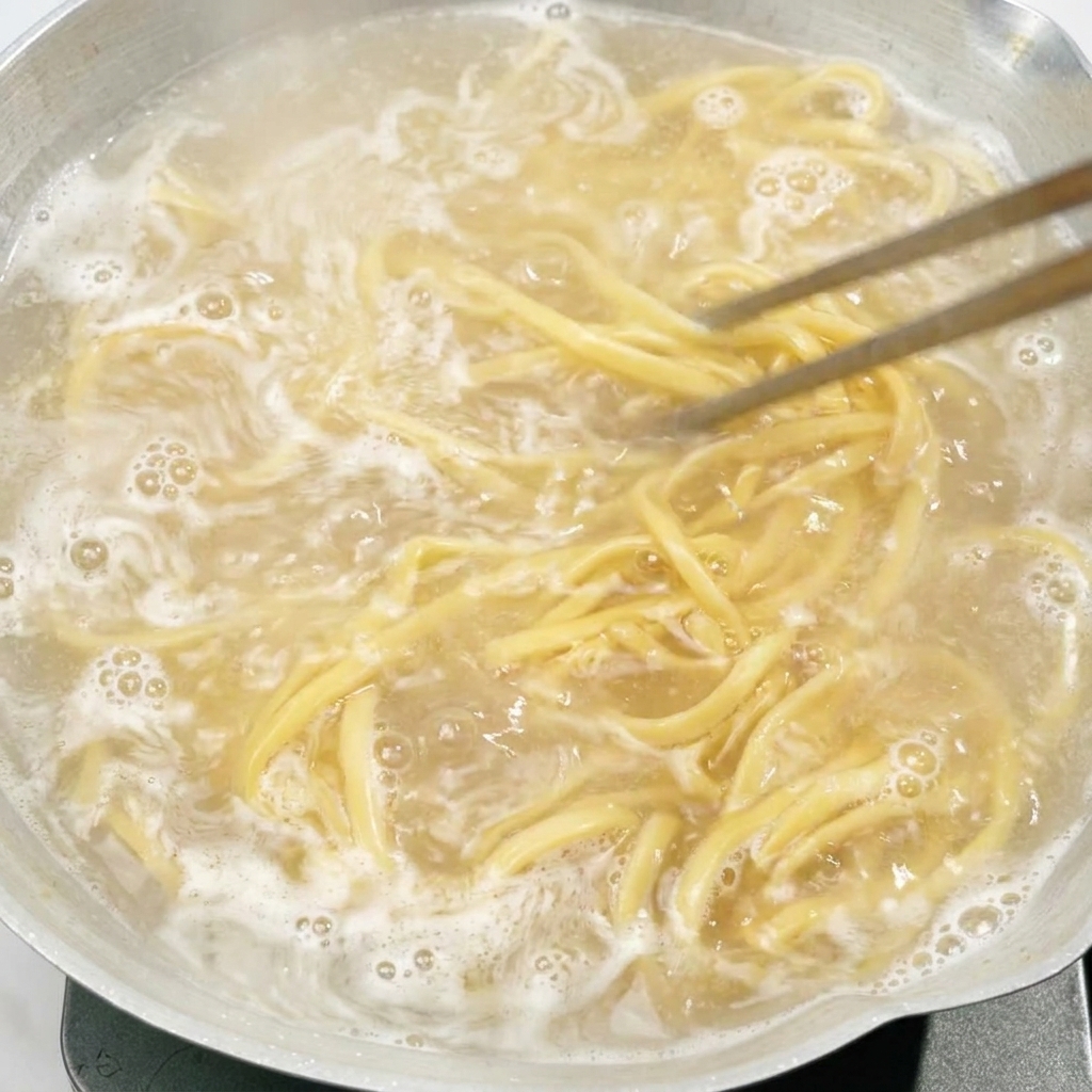 Palillos removiendo fideos que hierven en una olla con agua.