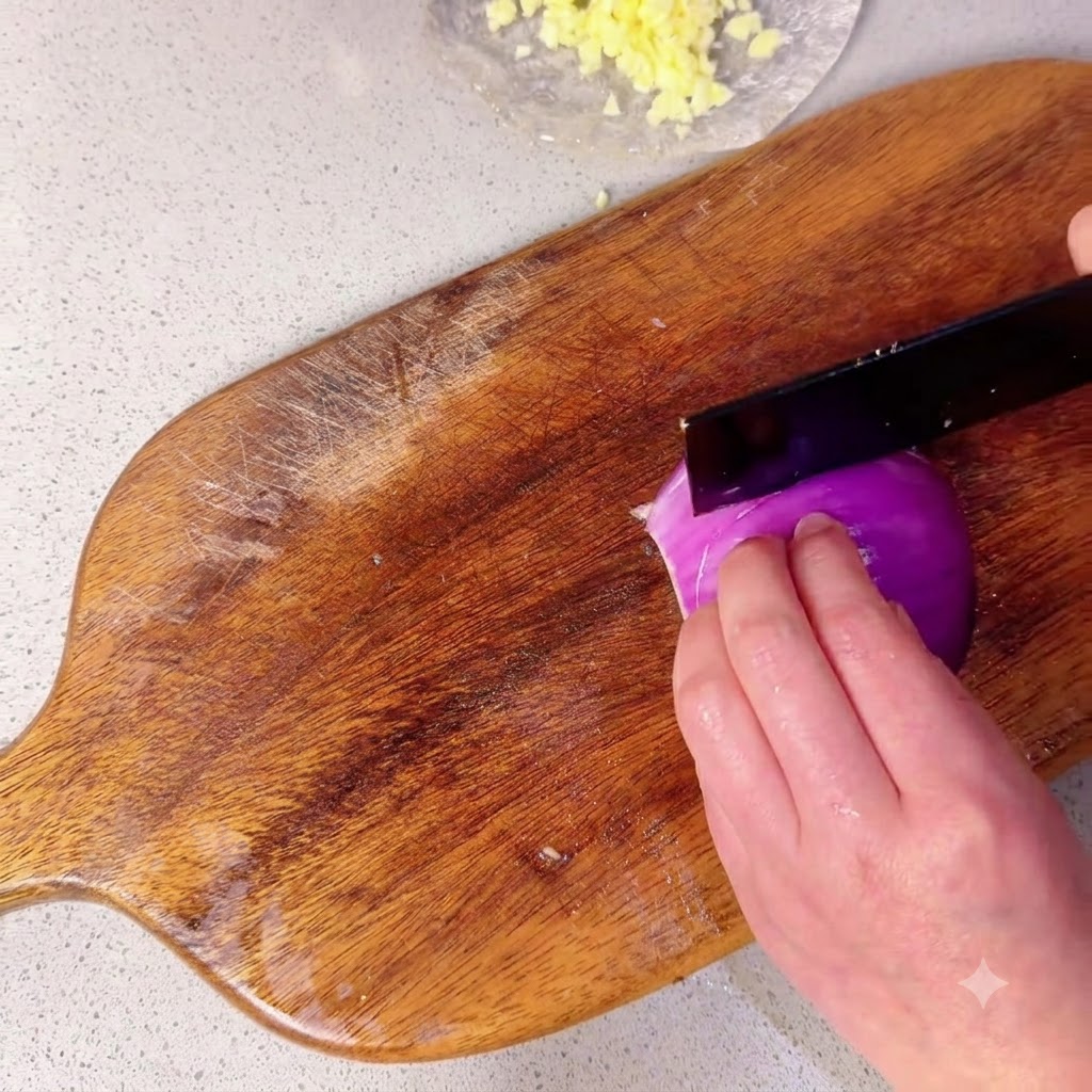 Mitad de una cebolla morada siendo cortada en trozos pequeños sobre una tabla de cortar de madera.