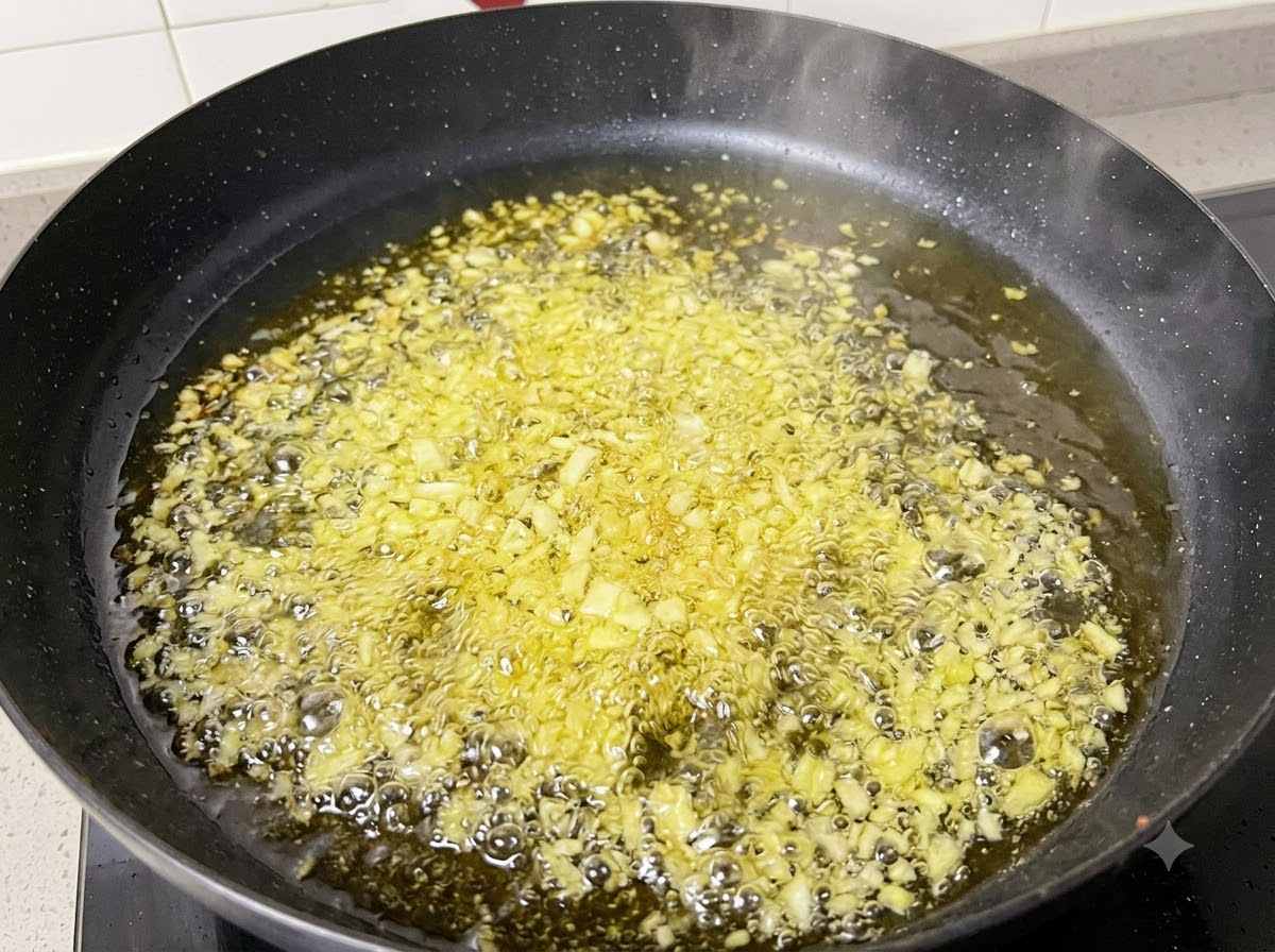 Ajo picado y cebollas friéndose y burbujeando en aceite caliente dentro de una sartén negra.