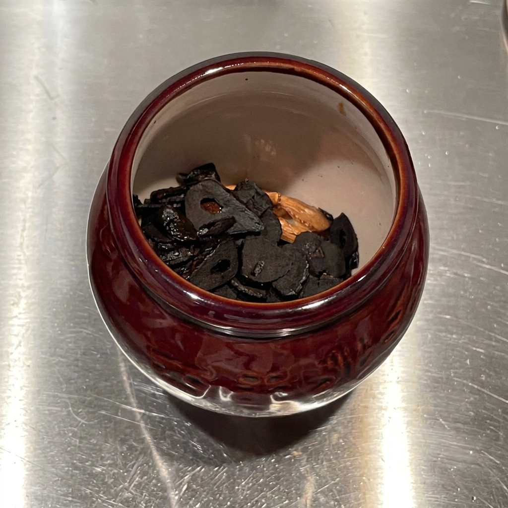 Aceite infusionado con ajo vertiéndose desde arriba en un mortero de cerámica lleno de chips de ajo frito.
