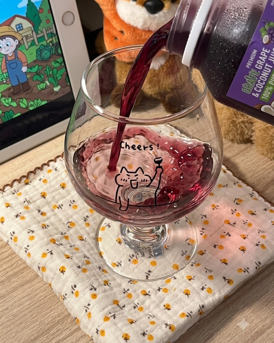 Zumo de uva morado oscuro siendo vertido desde un cartón en una copa de cristal transparente con el diseño de un gato animado.