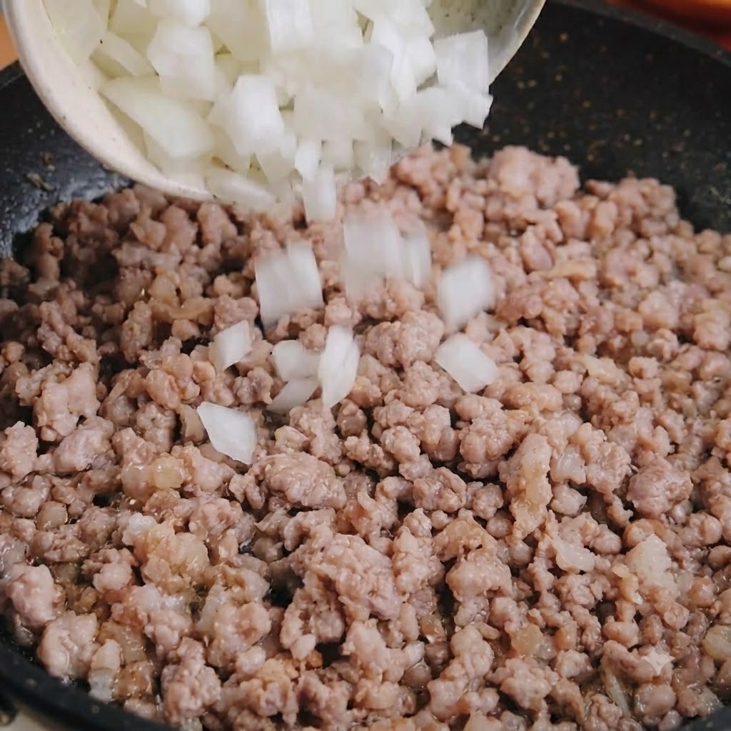 Cebolla blanca en cubitos vertida desde un tazón en una sartén de cerdo picado cocinado.