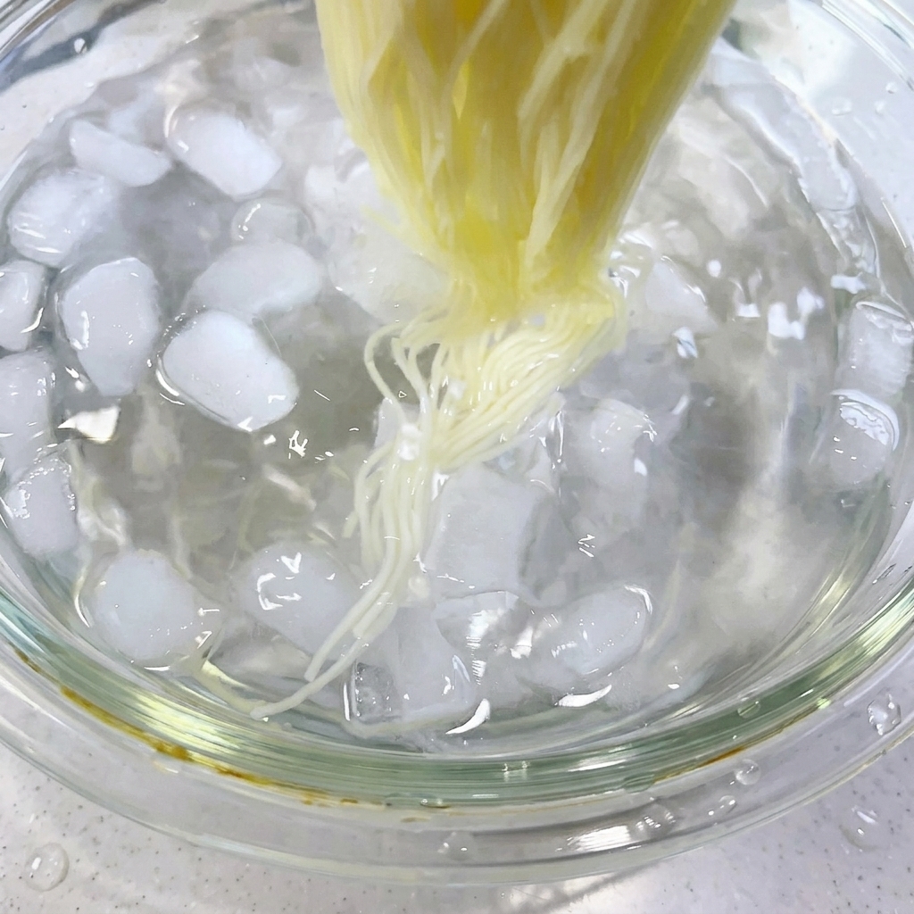 Palillos removiendo fideos cocidos en un baño de agua helada lleno de cubitos de hielo.