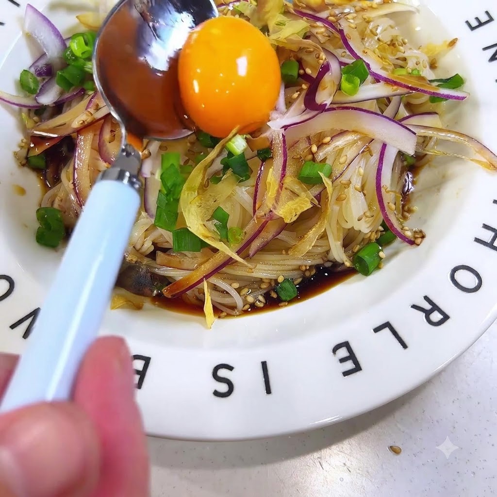 Una brillante yema de huevo cruda apoyada en una cuchara colocada en el centro de los fideos somen aderezados.