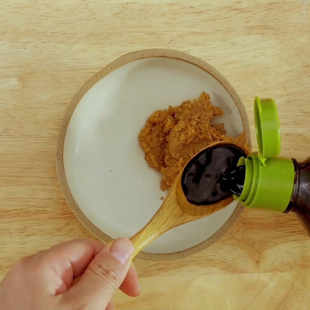 Salsa de soja oscura siendo vertida en un cuenco con pasta de miso rojo espesa.