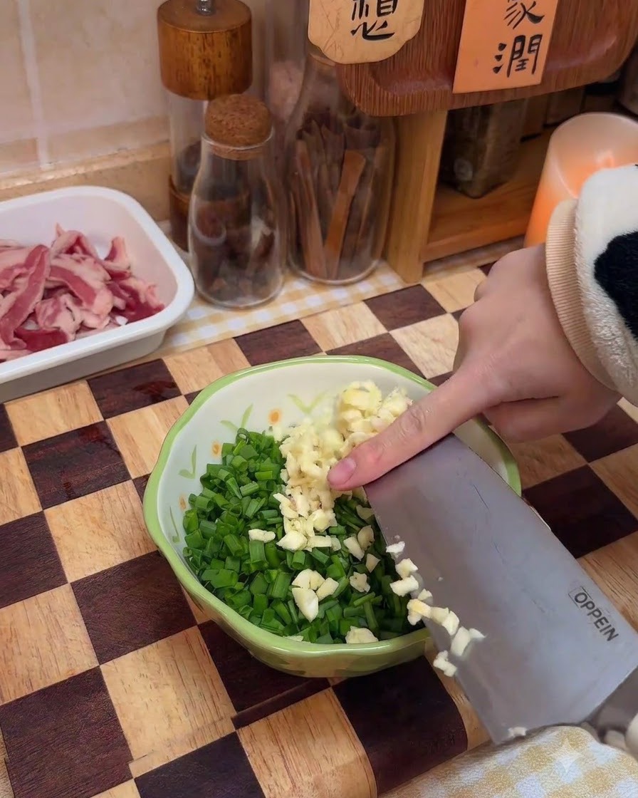 Ajo picado siendo añadido a un cuenco con cebolletas picadas y especias.