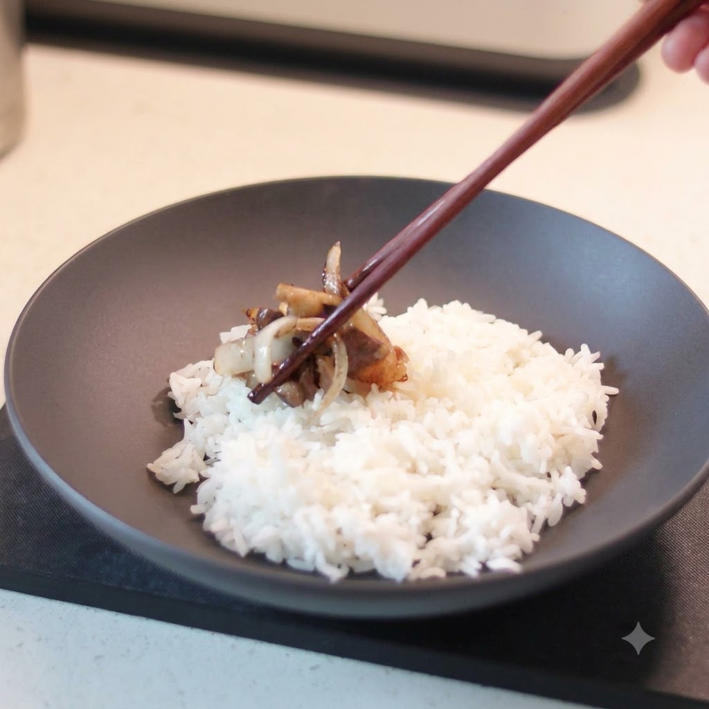 Un par de palillos de madera sosteniendo una porción de ternera cocinada y cebollas caramelizadas, colocándola en un tazón de cerámica oscura lleno de arroz blancocite: 1.