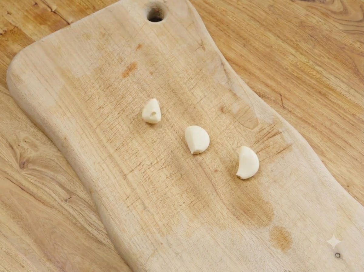 Tres dientes de ajo pelados reposando sobre una tabla de cortar de madera.