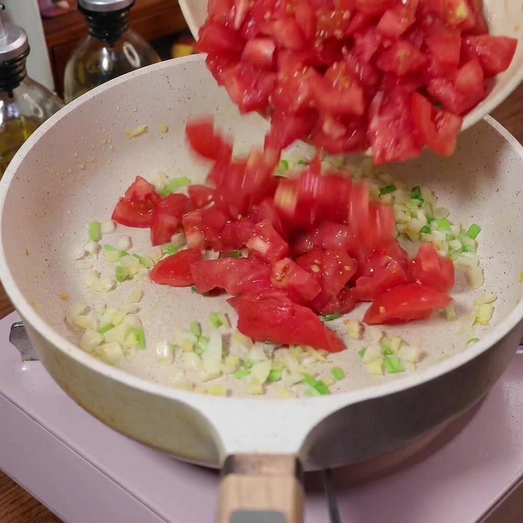 Tomates en dados siendo vertidos en una sartén con los aromáticos sofritos.