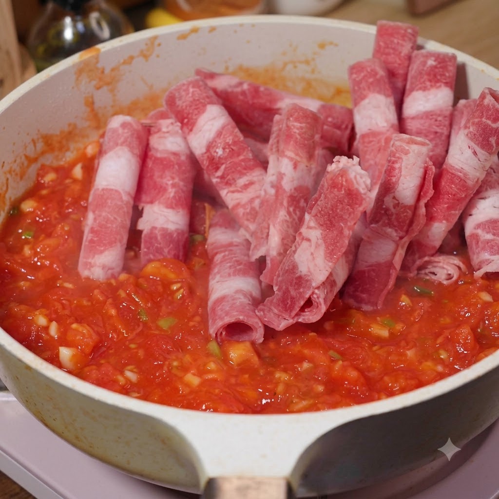 Ternera grasa en lonchas siendo añadida a una sartén con tomates para ser salteada.