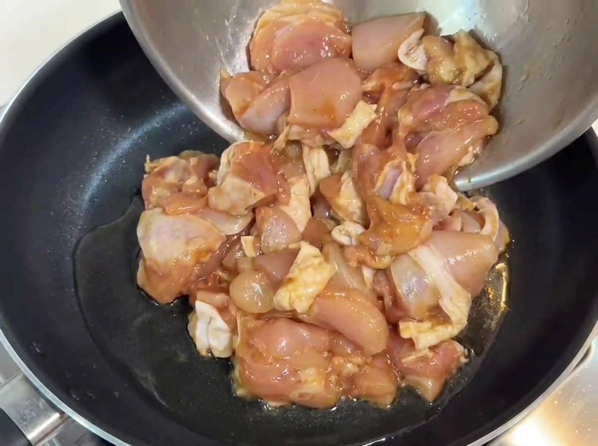 Trozos de pollo marinados siendo vertidos en una sartén con aceite caliente.