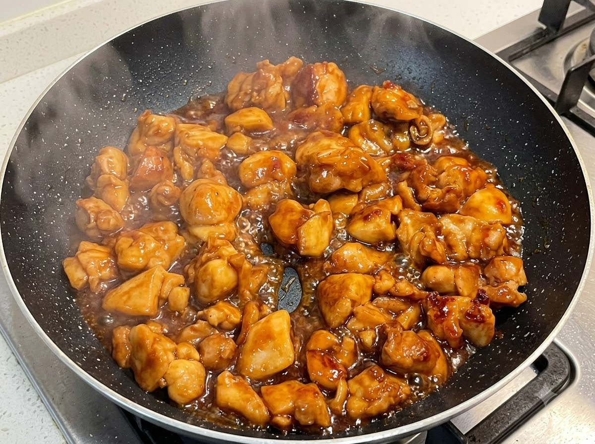 Pollo cocinándose a fuego lento en una salsa espesa dentro de una sartén.