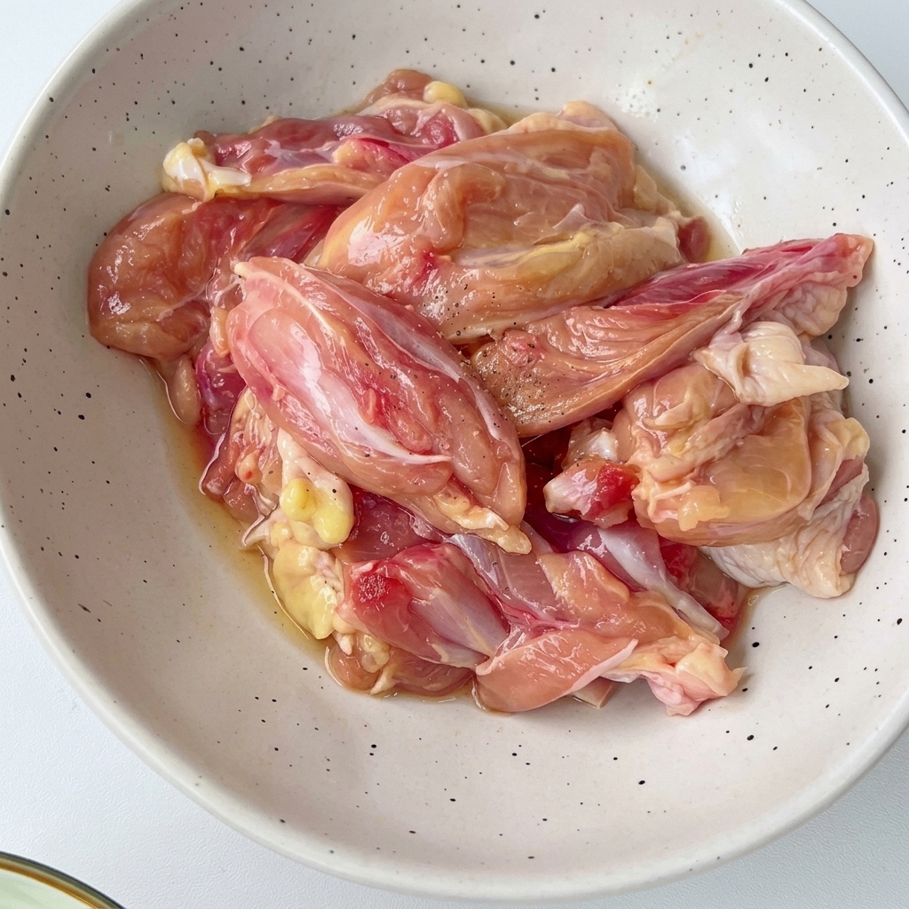 Trozos de pollo picados dentro de un bol blanco salpicado mezclados con condimentos y aromaticos.