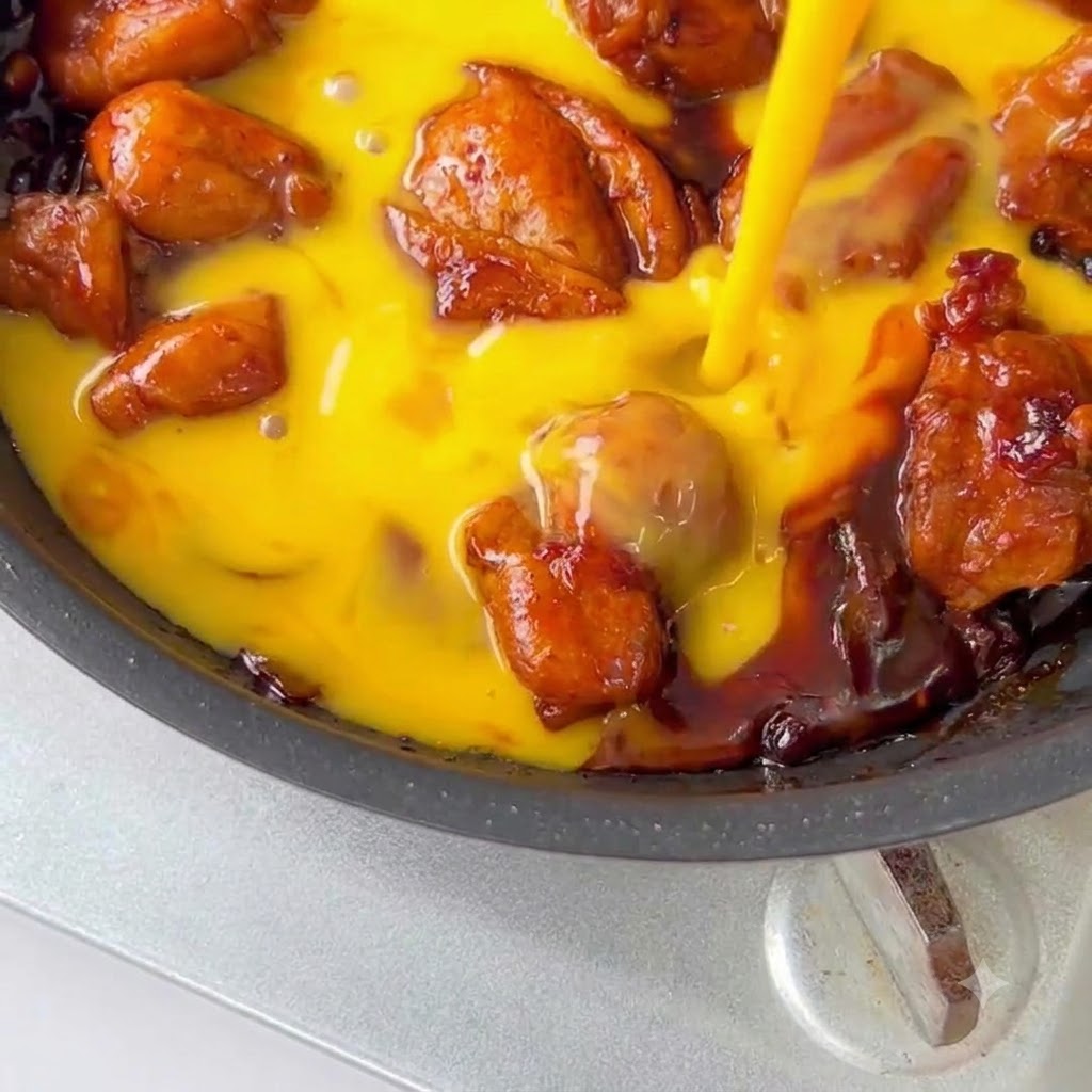 Mezcla de pollo y huevo decorada con semillas de sesamo y cebollino verde en una sartén.