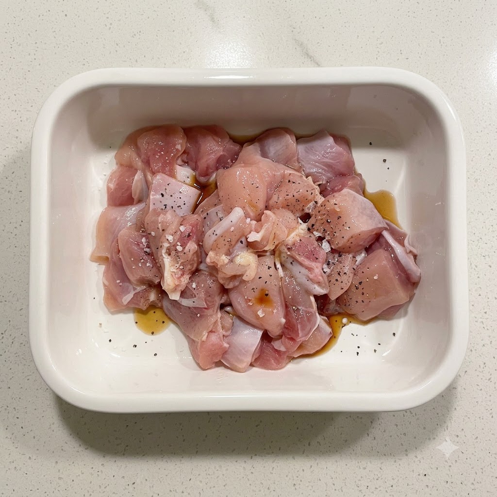 Trozos de pollo crudo sazonados con almidón, salsa de soja y pimienta negra dentro de un recipiente de cerámica blanco.