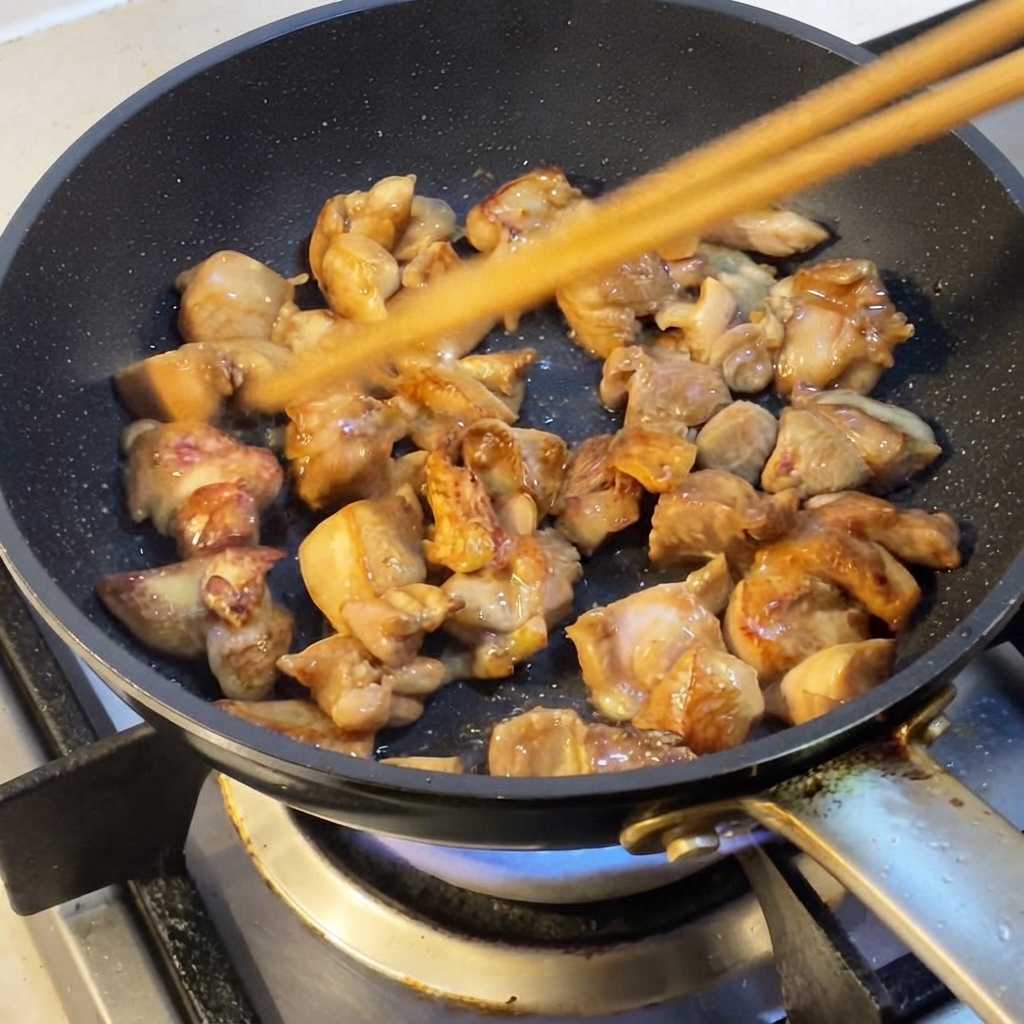 Trozos de pollo salteados en una sartén con palillos.