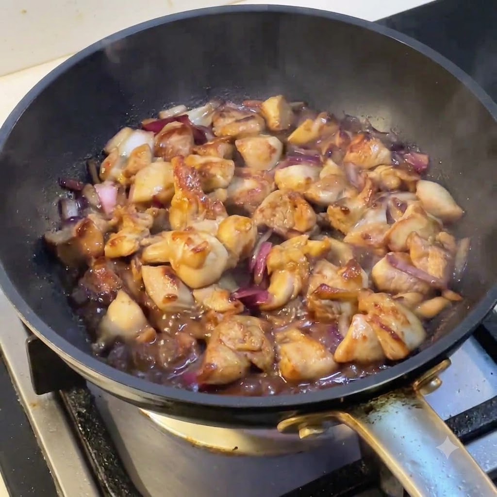 Una sartén llena de pollo y cebollas cocinándose a fuego lento mientras sale vapor de la superficie.