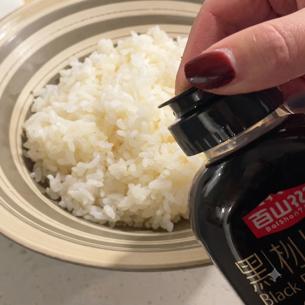 Salsa de trufa negra rociada desde una botella sobre un tazón de arroz blanco esponjoso al vapor.