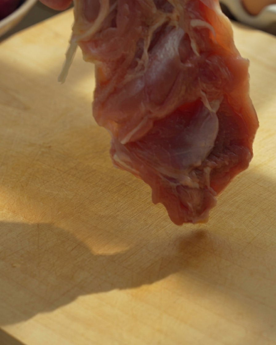 Contramuslos de pollo deshuesados cortados en trozos grandes sobre una tabla de madera con un cuchillo.