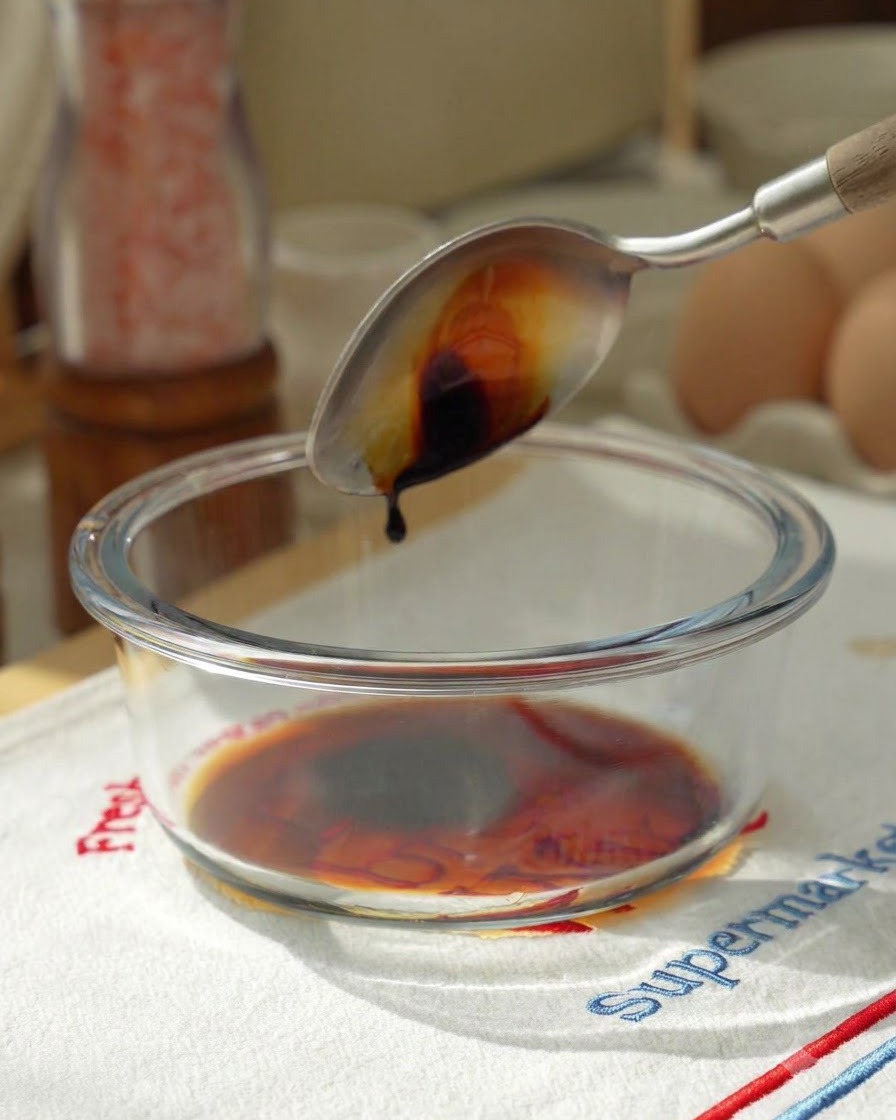 Vertiendo salsa de soja con una cuchara en un bol de cristal con los ingredientes de la salsa.