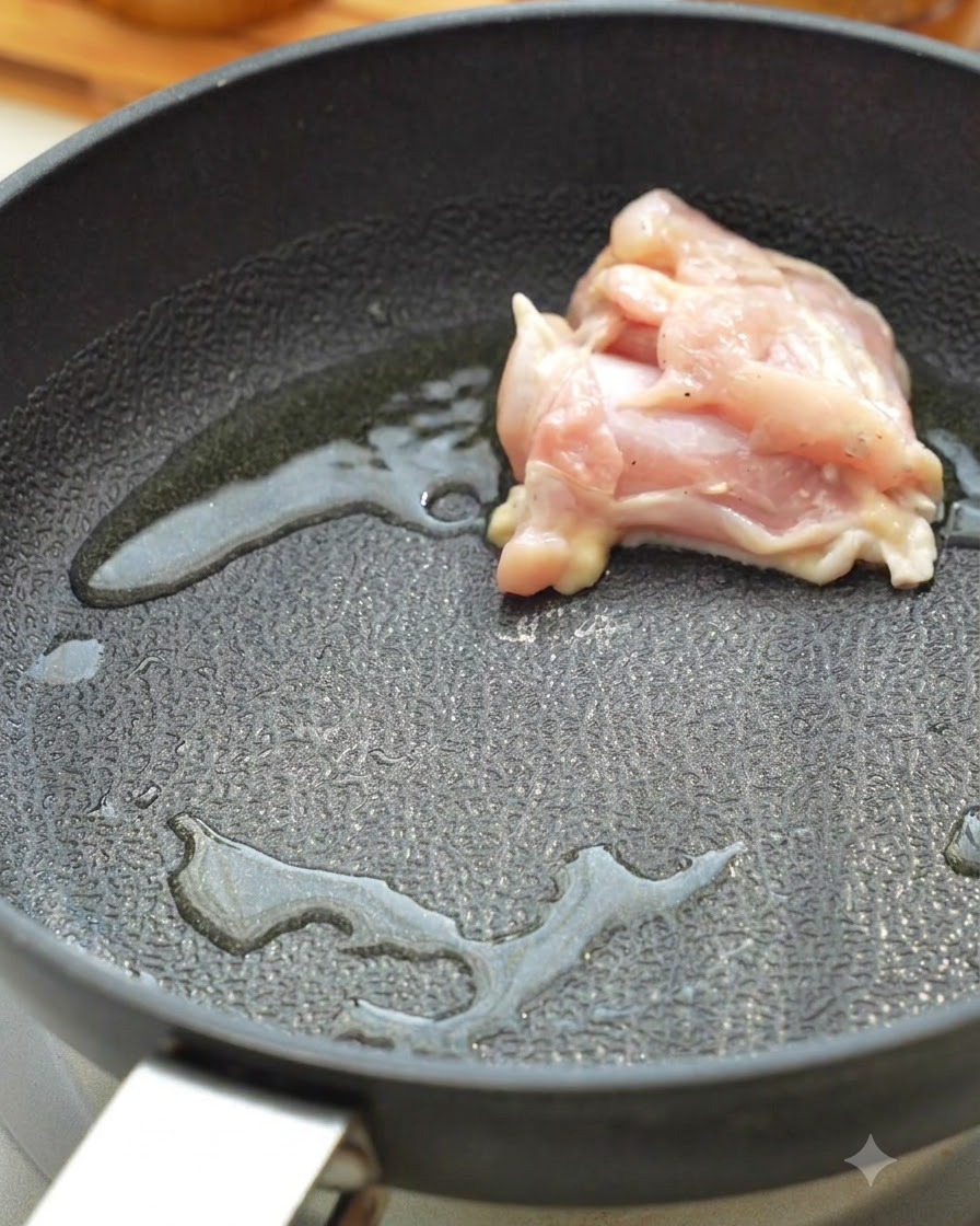 Trozos de contramuslo de pollo crudo dorándose en una sartén caliente con aceite.