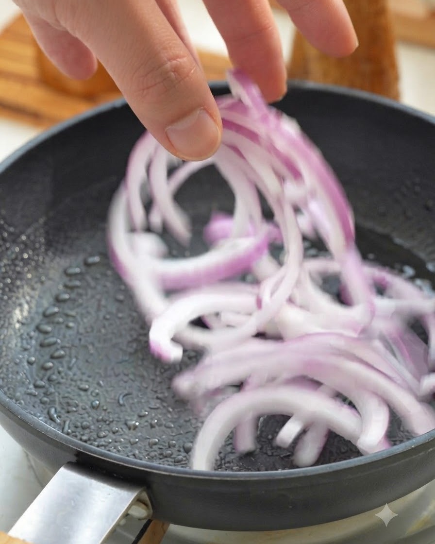 Cebolla morada en tiras salteándose en una sartén caliente.