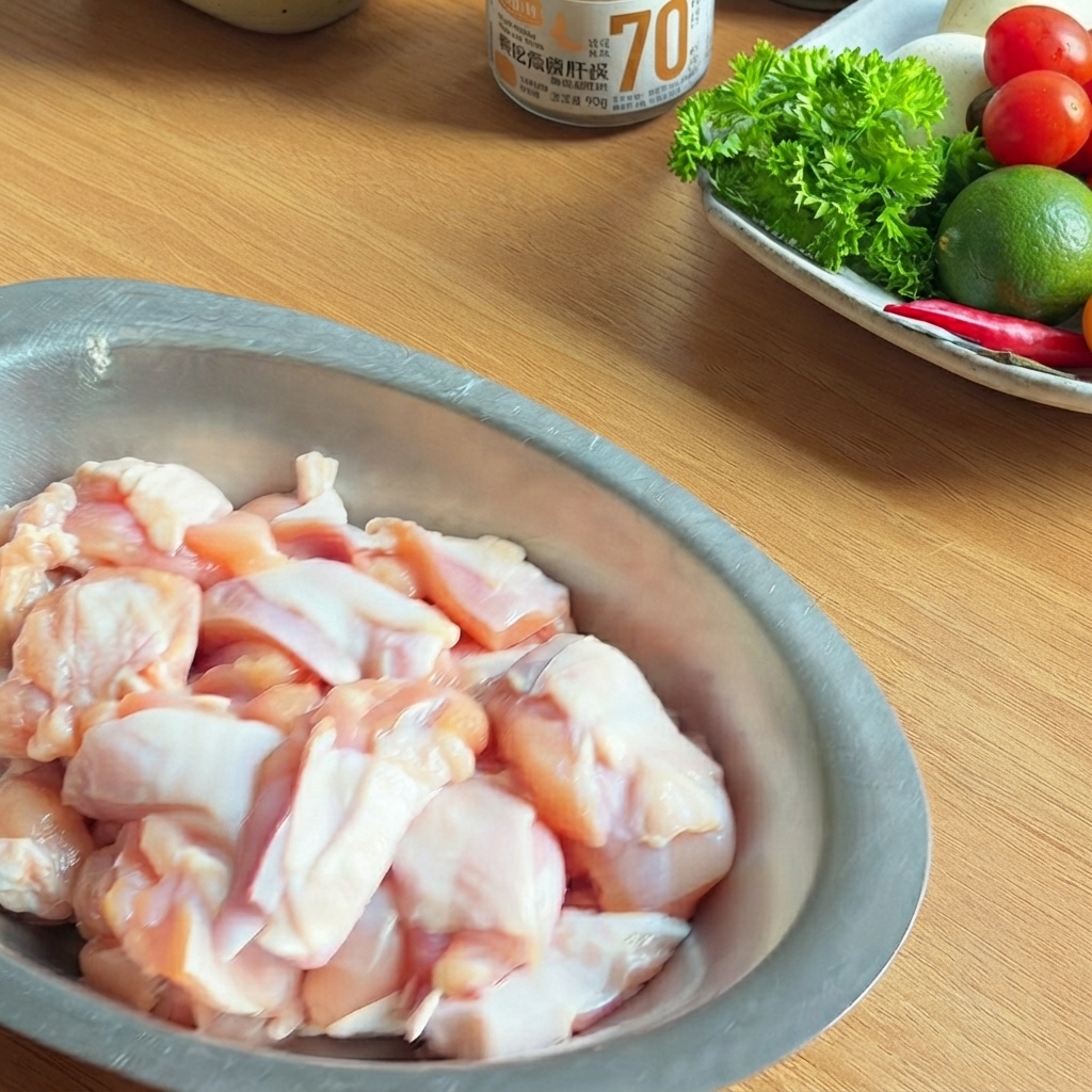 Un bol de metal lleno de trozos de pollo crudo sazonados con salsa de soja oscura, salsa de ostras y pimienta negra.