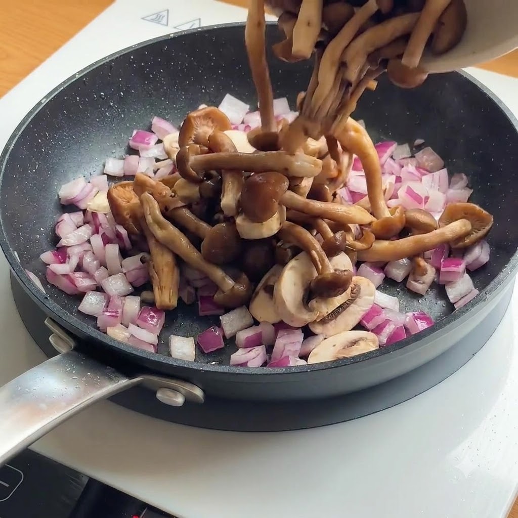 Rodajas de champiñones y cebollas moradas siendo añadidas a una sartén con trozos de pollo ya dorados.