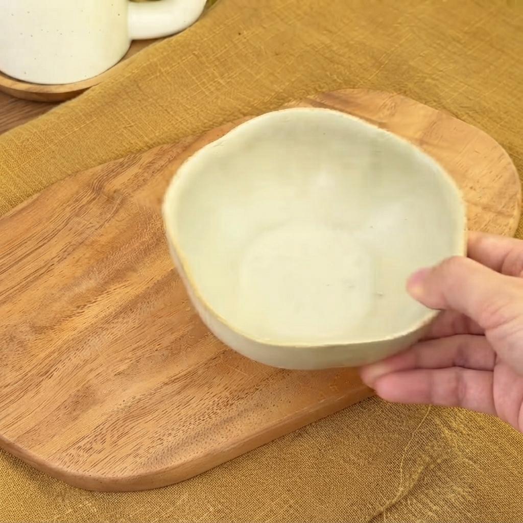 Un pequeño bol de cerámica vacío sostenido sobre una tabla de madera listo para mezclar la salsa.