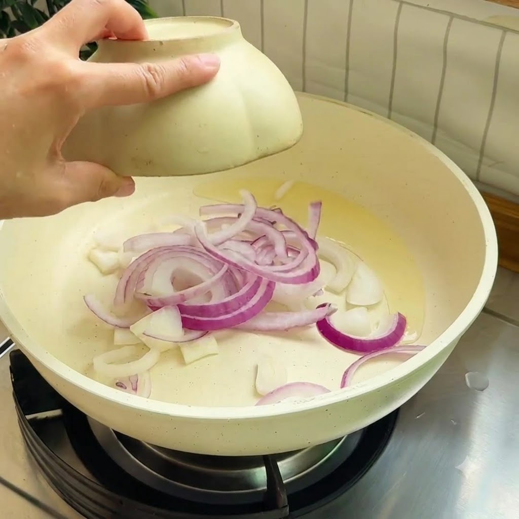 Tiras de cebolla morada salteándose en una sartén caliente con aceite de cocina.