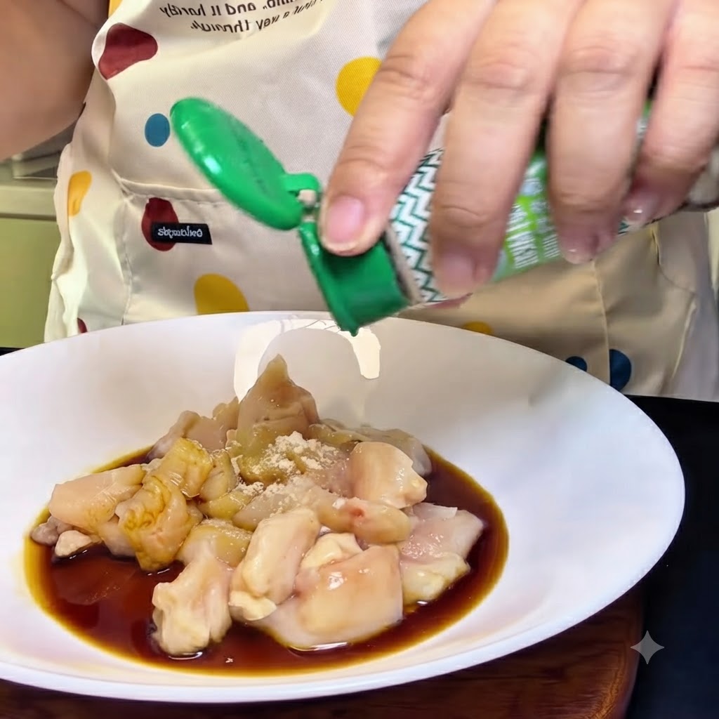 Una persona agitando un frasco de pimienta blanca sobre un bol blanco lleno de trozos de pollo crudo, salsa de soja y condimentos.