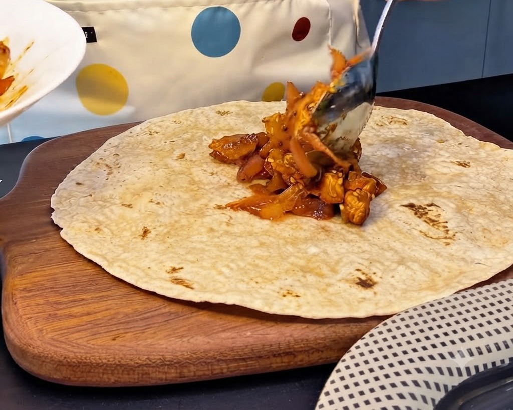 Una gran cucharada de relleno picante de pollo y kimchi siendo colocada en el centro de una tortilla integral.
