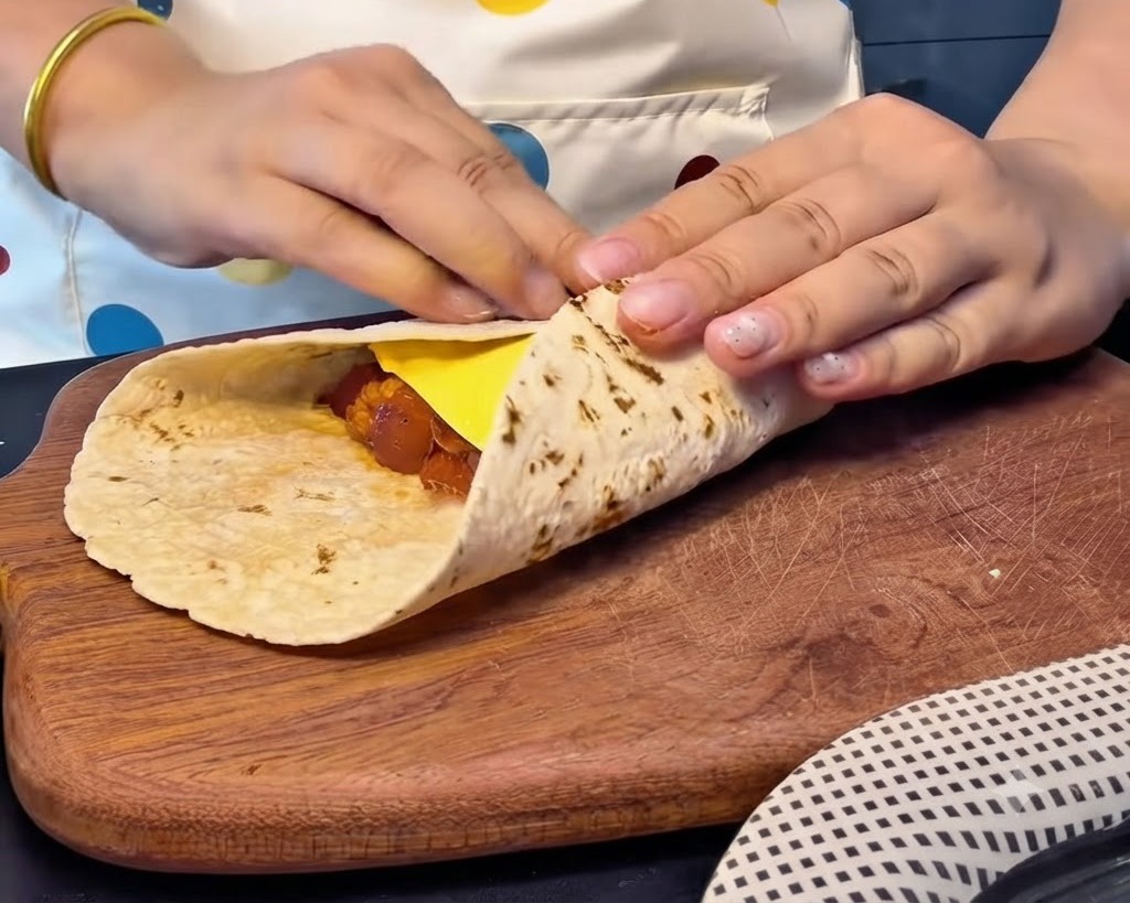 Manos doblando los bordes de un pan plano firmemente sobre una rebanada de queso y relleno para crear un paquete cuadrado sellado.