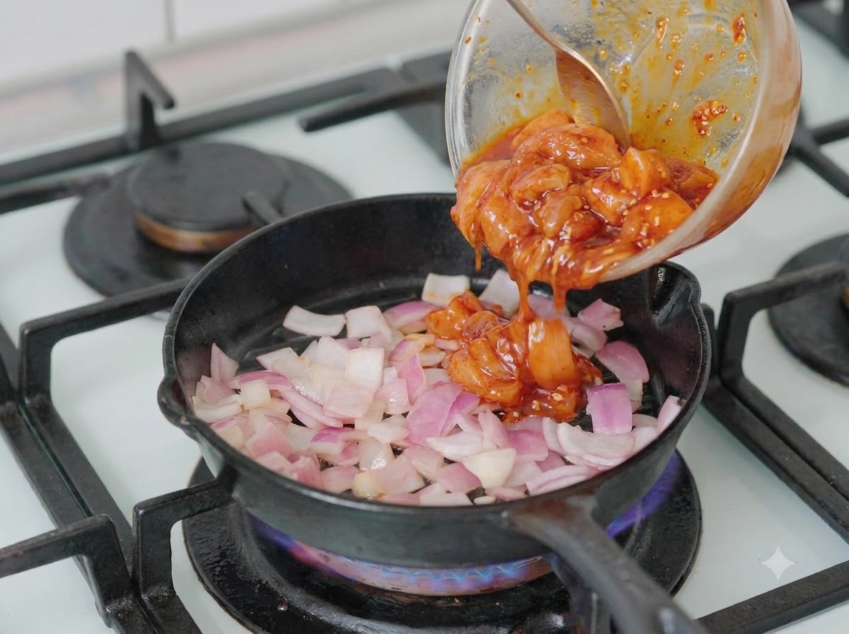 Trozos de pollo marinado vertiéndose desde un bol en una sartén que contiene cebollas picadas.