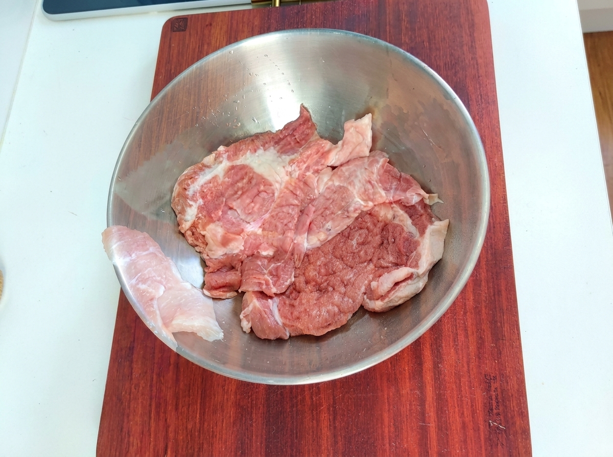 Trozos de cerdo en un tazón de mezcla de metal con ingredientes de adobo.