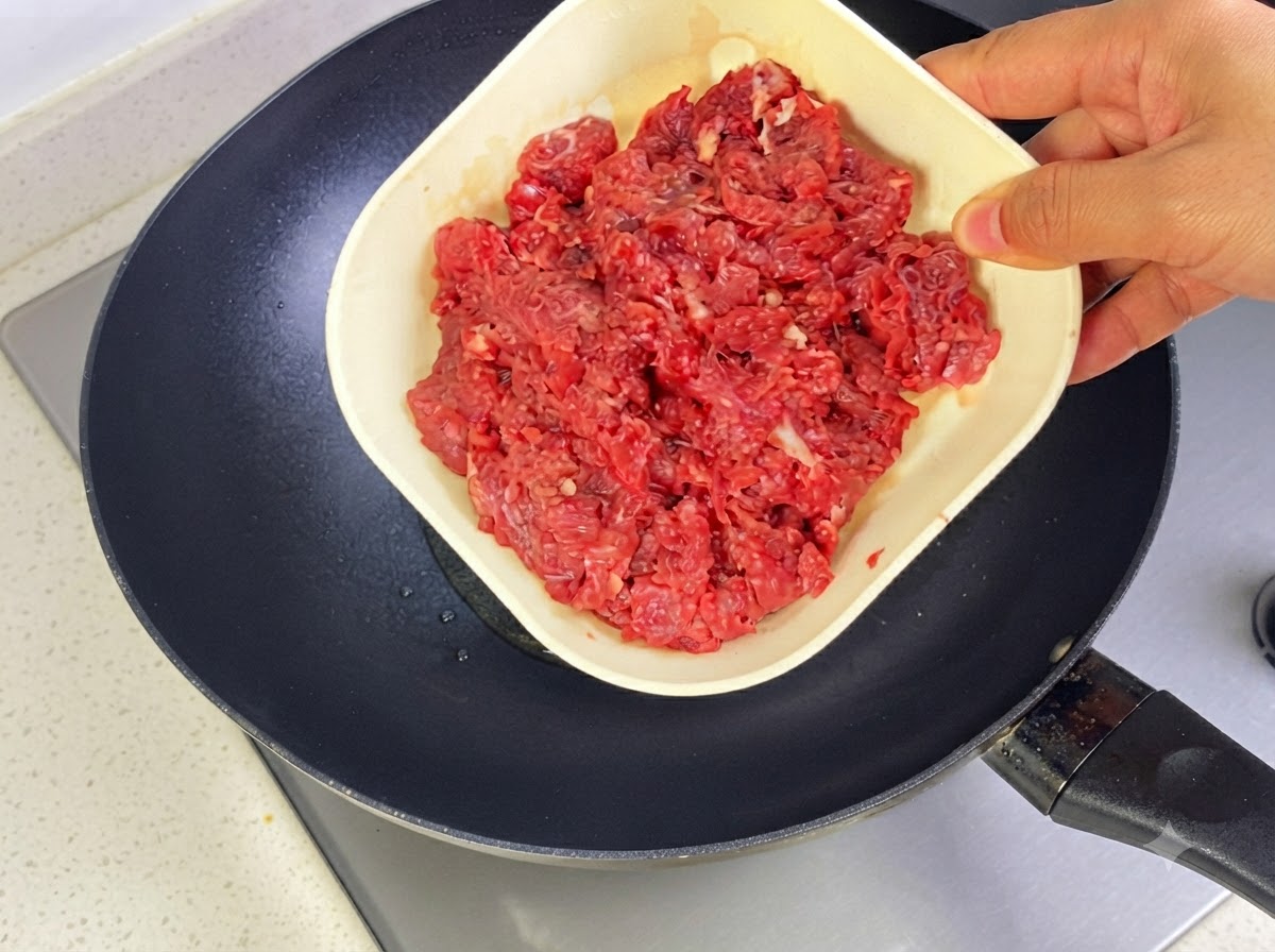 Carne de res molida siendo agregada a una sartén caliente con aceite para sofreír.