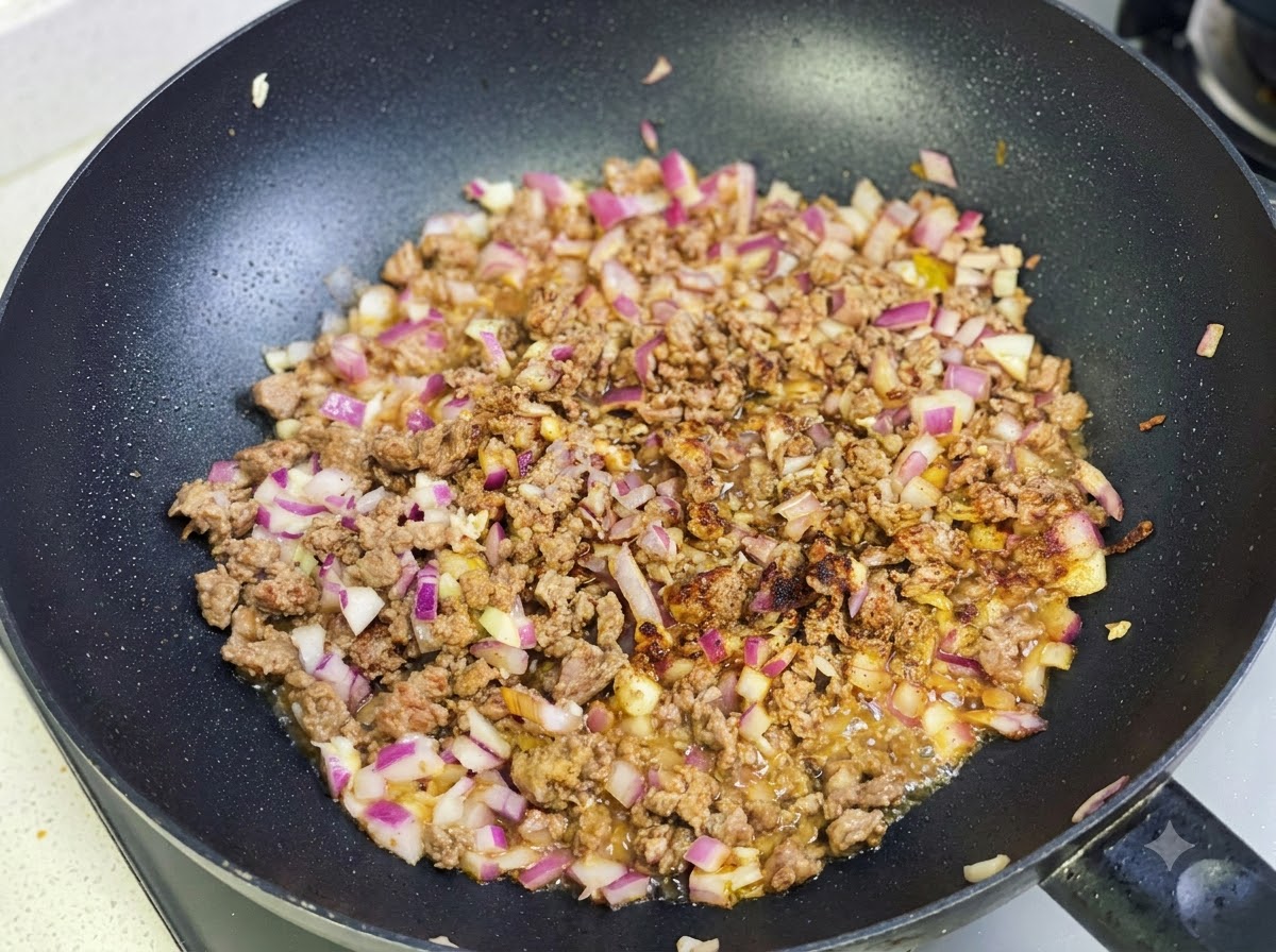 Pasta de curry y especias siendo salteadas con la mezcla de carne y cebolla en la sartén.