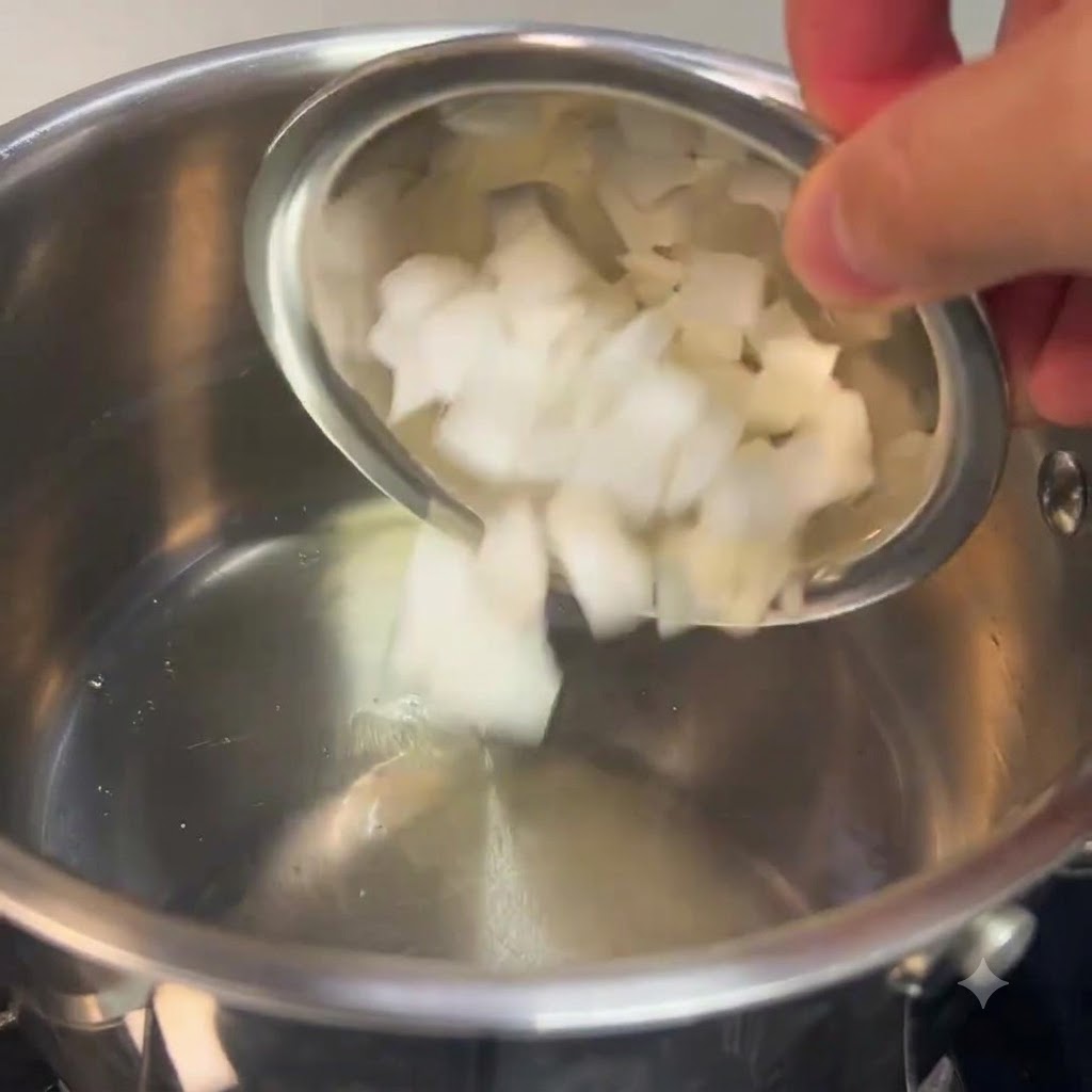 Cebollas blancas picadas siendo vertidas desde un tazón pequeño en una olla de acero inoxidable.
