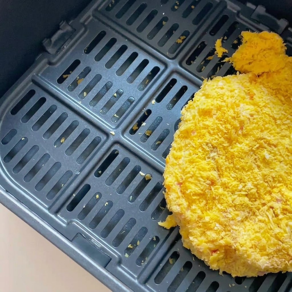 Una chuleta de cerdo empanada dentro de la canasta oscura de una freidora de aire.